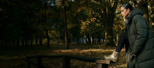 Woman in a green coat foot on a wooden bench in a forest during autumn, wearing grubs boots